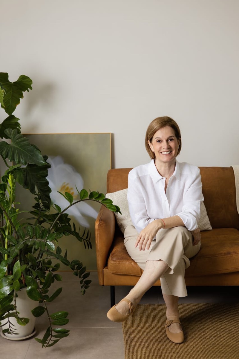 Denise Pinto, founder of Zeyra Journeys, seated on a sofa surrounded by plants.